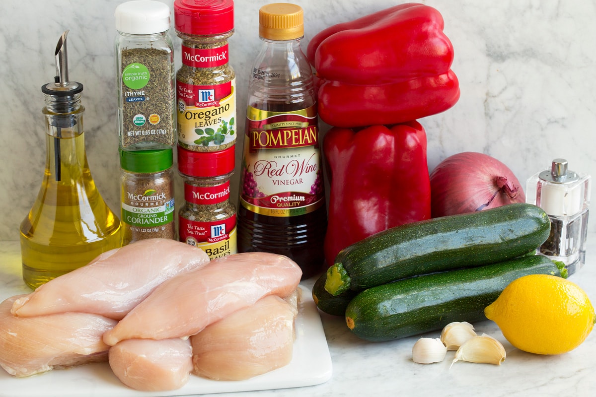 Ingredients that are used to make chicken kebabs shown in this image. Includes chicken breasts, herbs, vinegar, oil, lemon, and fresh vegeables.