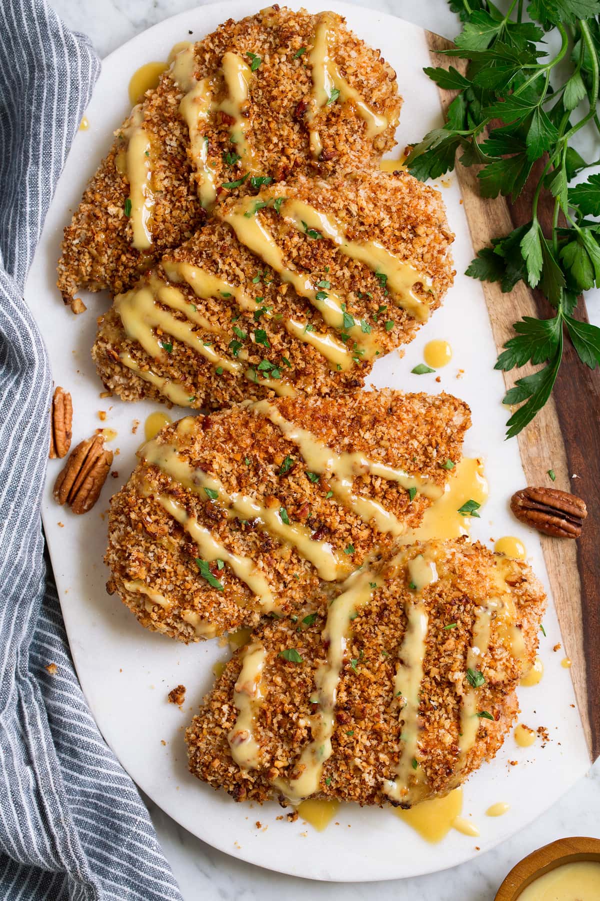 Chicken with pecan and panko breadcrumbs on a marble serving platter. Chicken is drizzled with honey mustard sauce.