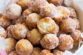Homemade donuts in a serving bowl. Two are bitten into to show texture of interior.