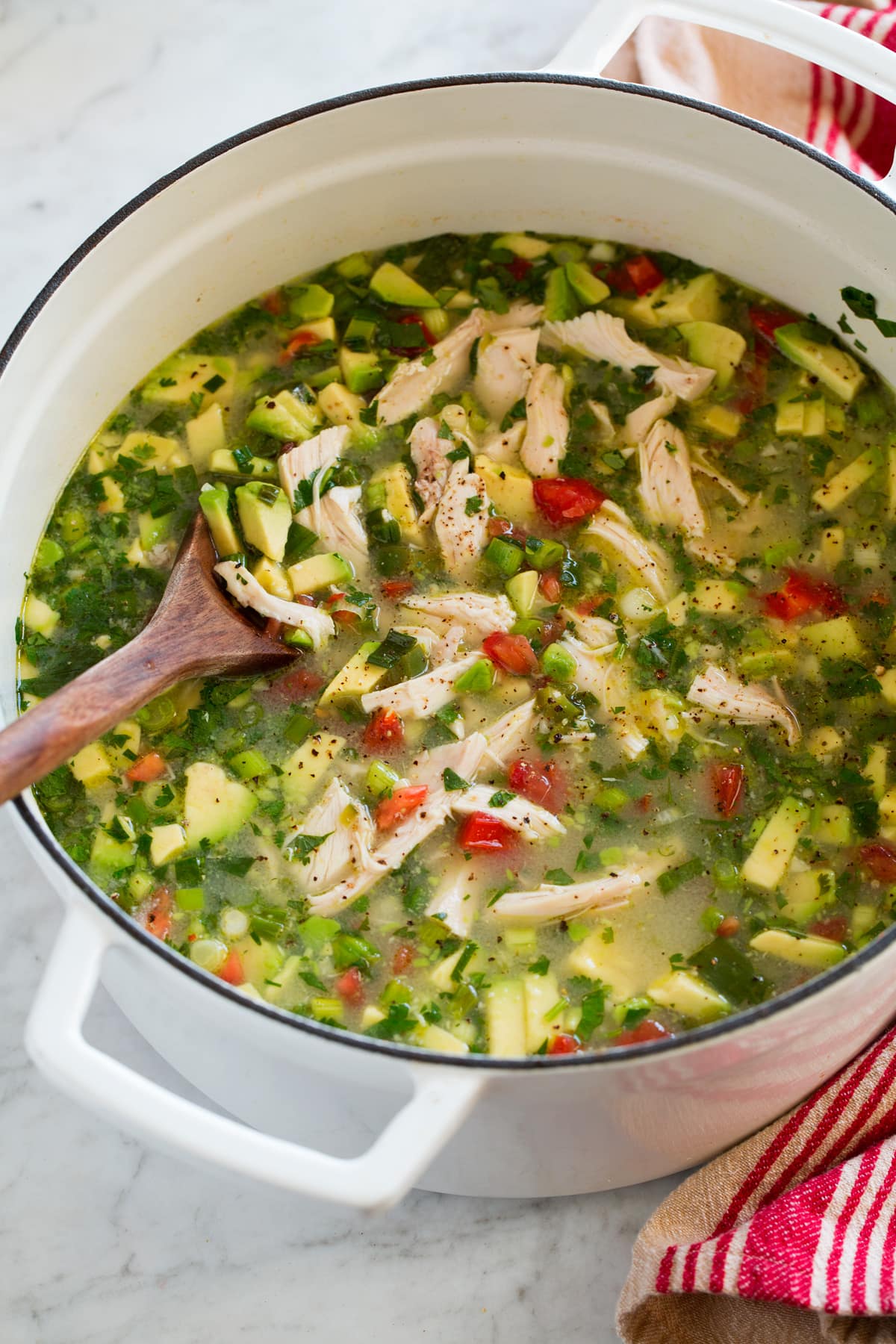 White pot filled with chicken soup with avocado and tomatoes.