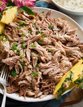 Kalua pork shown in a serving bowl with pineapple and rice to the side.