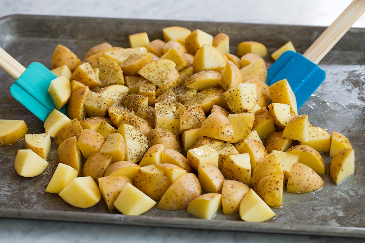 Tossing potatoes with oil, lemon and seasonings using silicone spatulas. Potatoes are on a alluminum baking sheet.