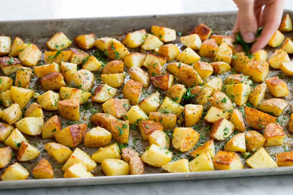 Hand sprinkling roasted potatoes with parsley.