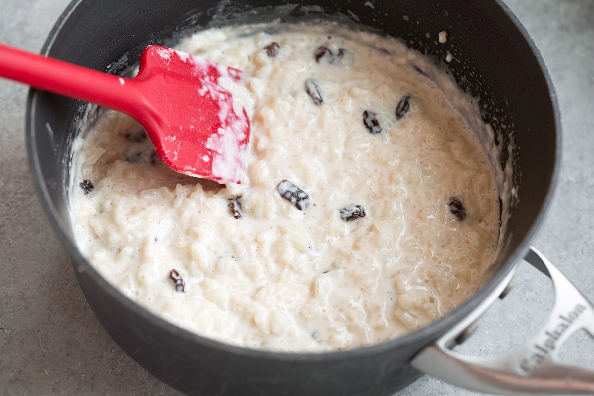 Rice pudding shown once finished cooking in saucepan with raisins added.