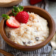 Rice Pudding in a small wooden bowl. It is garnished with cinnamon and strawberries.
