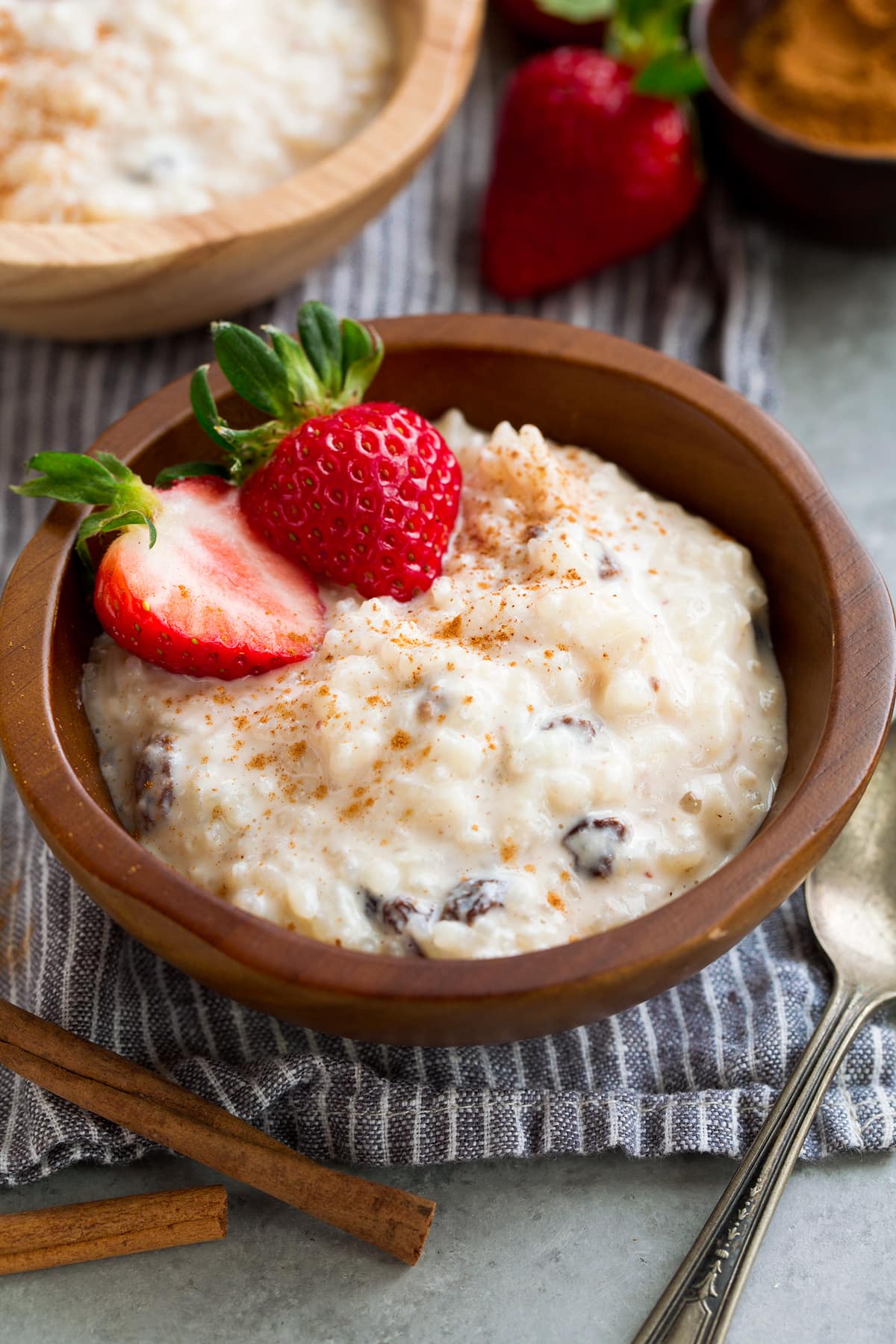 Rice Pudding in a small wooden bowl. It is garnished with cinnamon and strawberries.