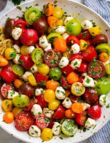 Tomato Salad in a white serving bowl. Shown in salad are multi-color cherry tomatoes and grape tomatoes, mozzarella pearls and it's coated in a herb dressing.