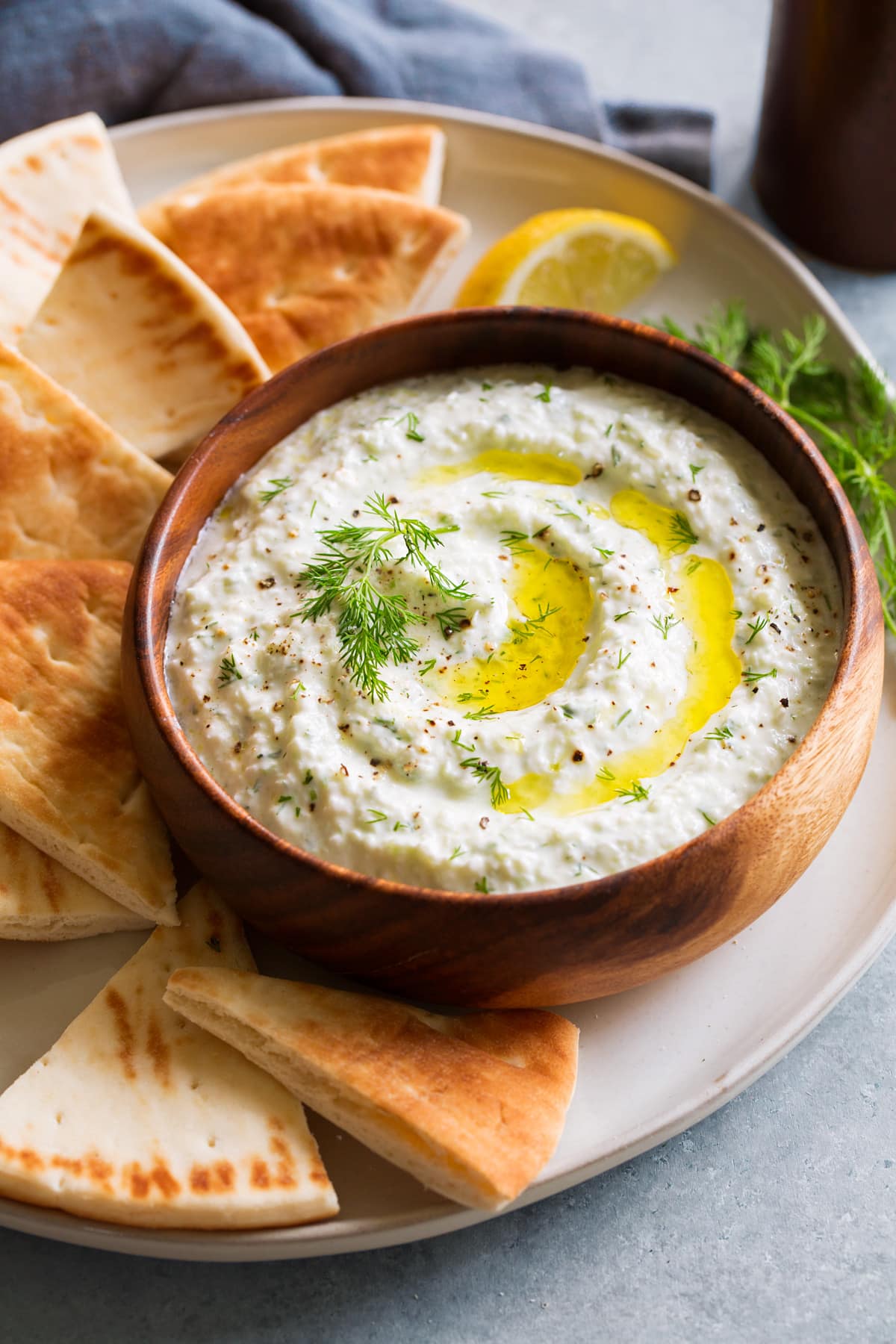 Bowl of homemade tzatziki sauce in wooden bowl on a platter with pita bread to the side.
