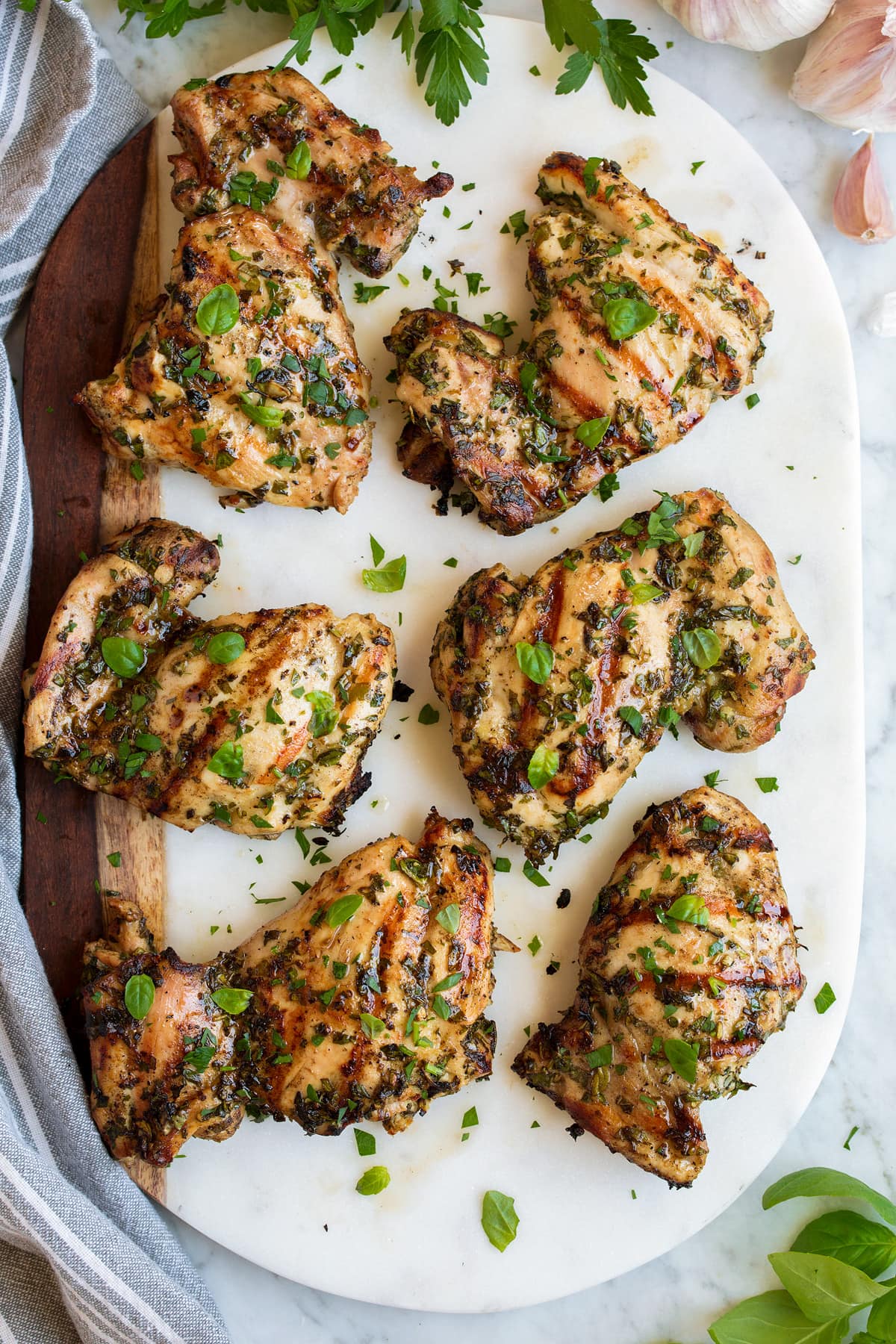 Six pieces of Garlic Herb Grilled Chicken shown overhead resting on a marble and wooden platter. 