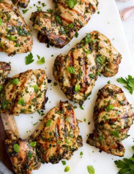Close up image of grilled chicken with herbs on a white platter.
