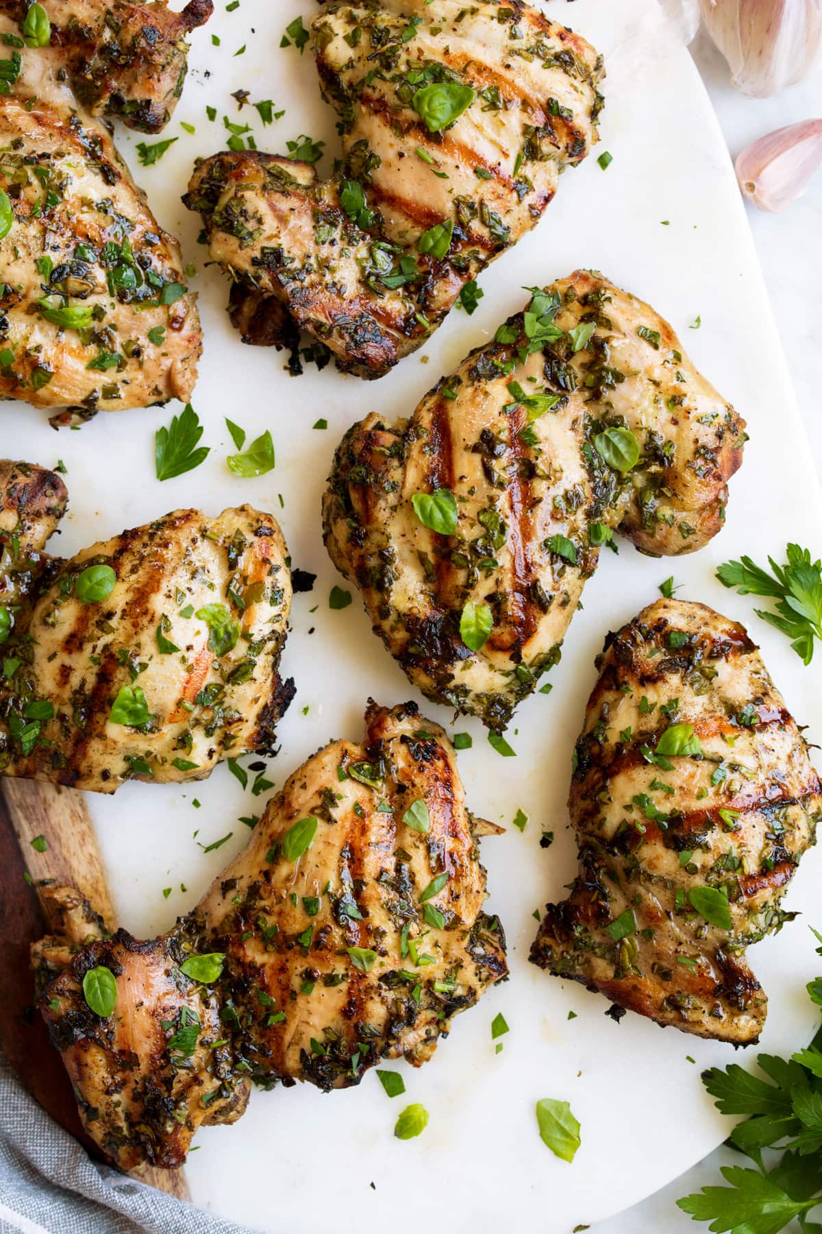 Close up image of grilled chicken with herbs on a white platter.