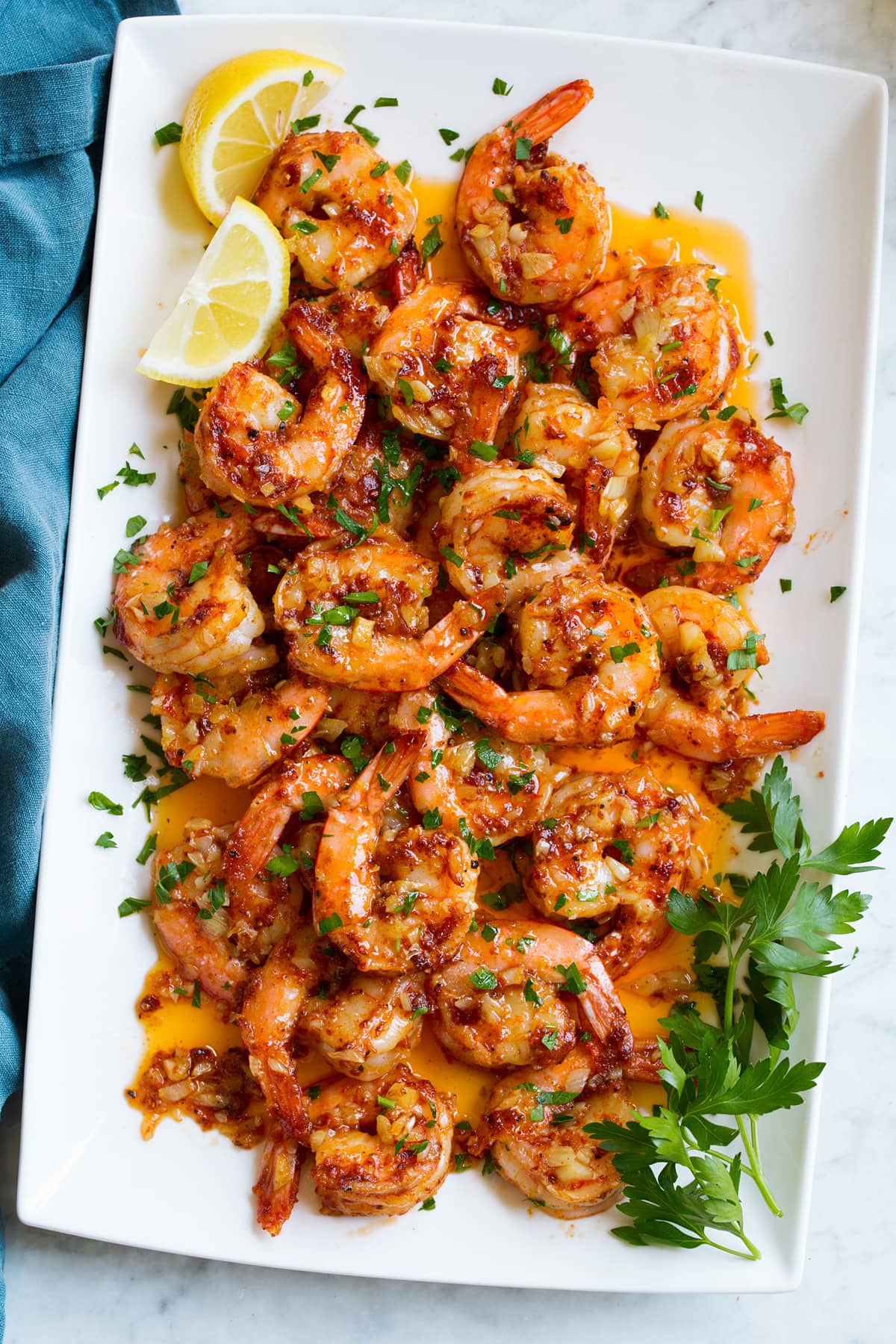 Overhead image of Hawaiian garlic shrimp on a white platter. It is garnished with fresh lemon wedges and parsley. 