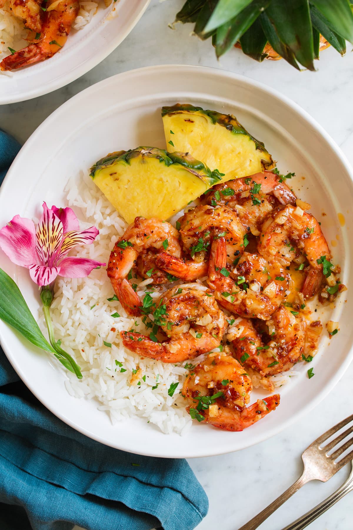 Garlic shrimp in a shallow white bowl with rice, pineapple and a fresh tropical flower for decoration.