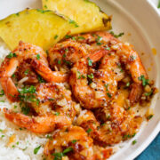 Close up image of Hawaiian garlic shrimp served over white rice with slices of fresh pineapple.