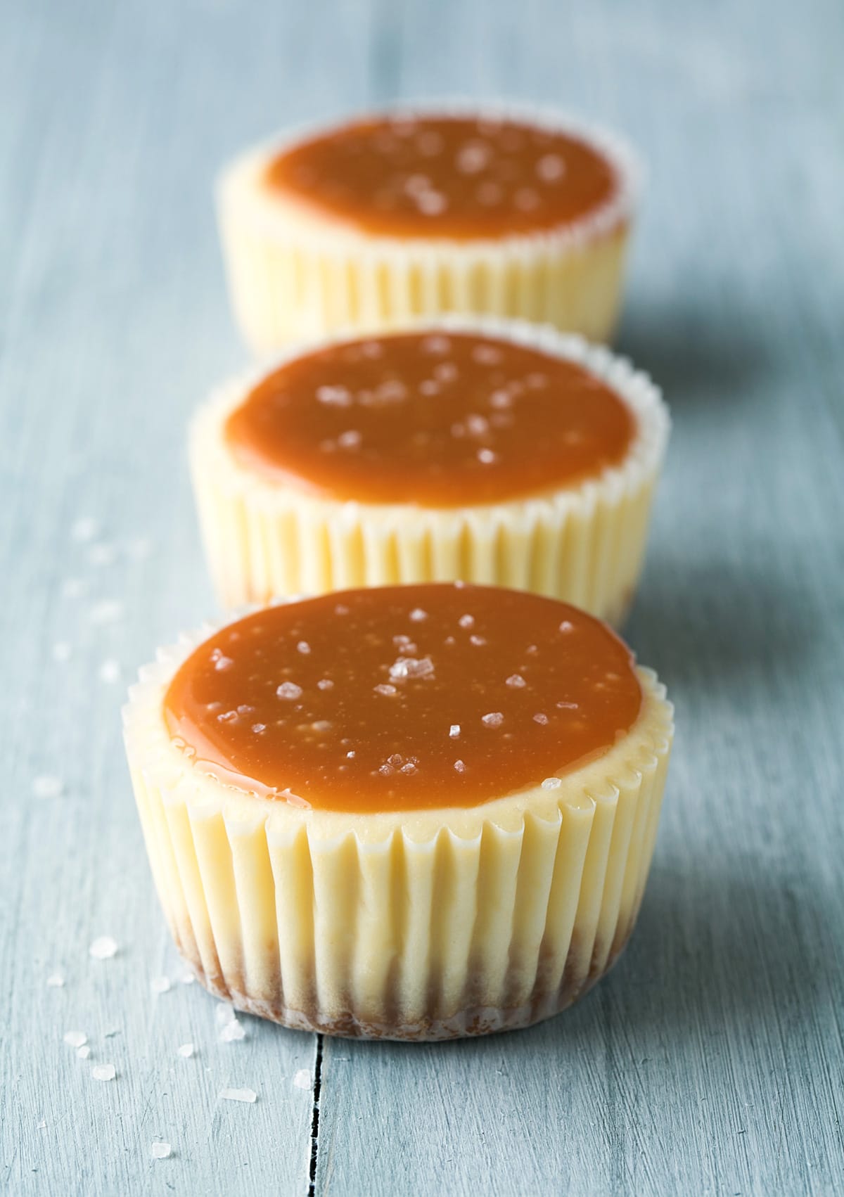 Three mini cheesecakes in a row topped with salted caramel sauce.