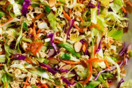 Close up overhead image of Asian ramen noodle salad in a large white salad bowl set over a marble surface.