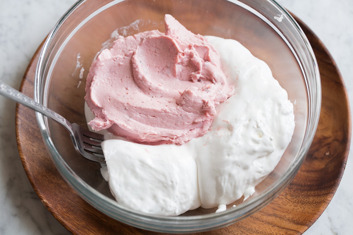 Marshmallow fluff and strawberry fruit dip in a glass mixing bowl shown before blending.