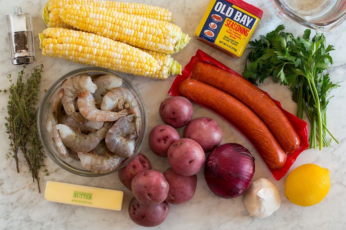 Image of ingredients used to make shrimp boil. Includes shrimp, corn on the cob, andouille sausage, red potatoes, onion, butter, lemon, parsley, thyme, garlic, salt and pepper and water.