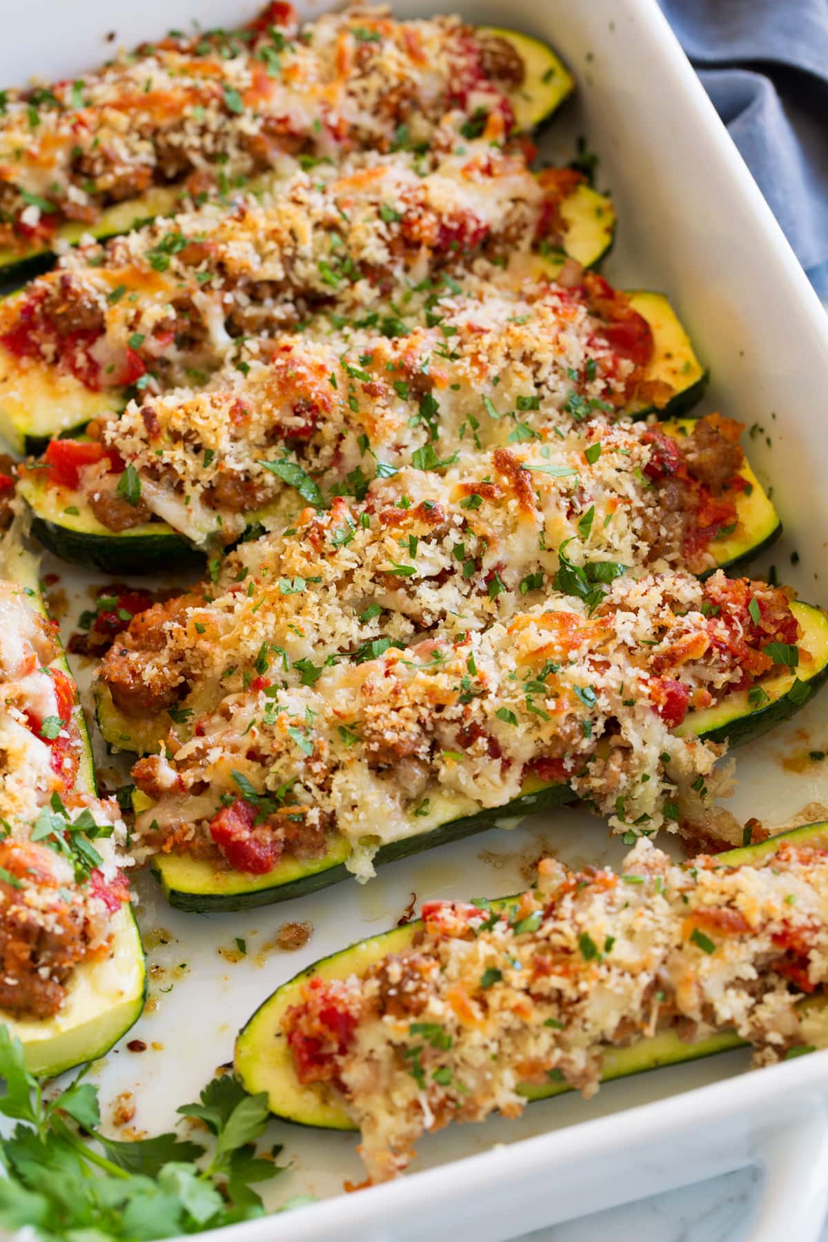 Image of zucchini boats stuffed with sausage, tomatoes, panko, and cheeses shown in a white baking dish.