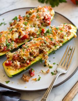 Two stuffed zucchini boats on a white dinner plate with a fork to the side.