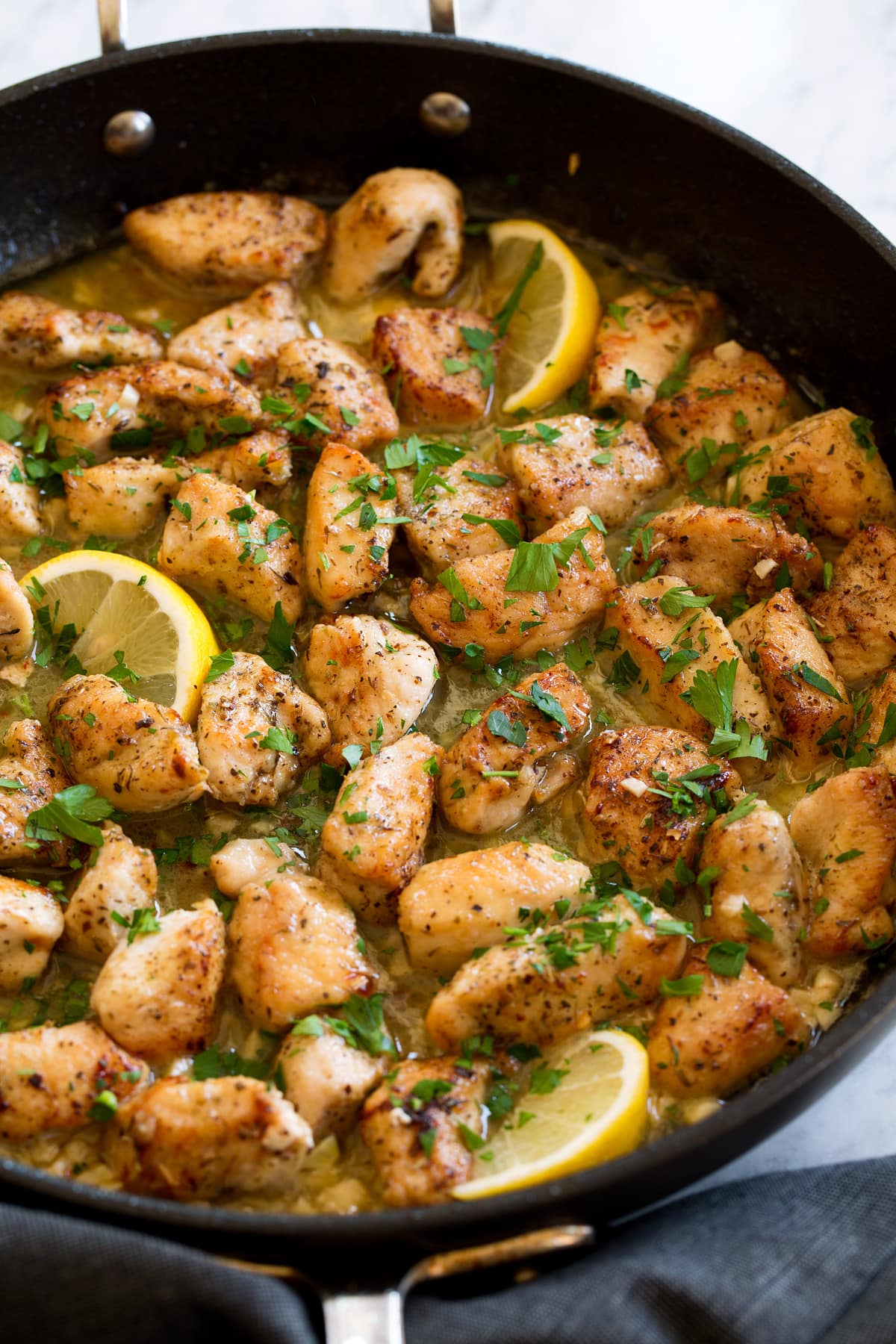 Chicken scampi with butter and wine shown in a dark skillet.