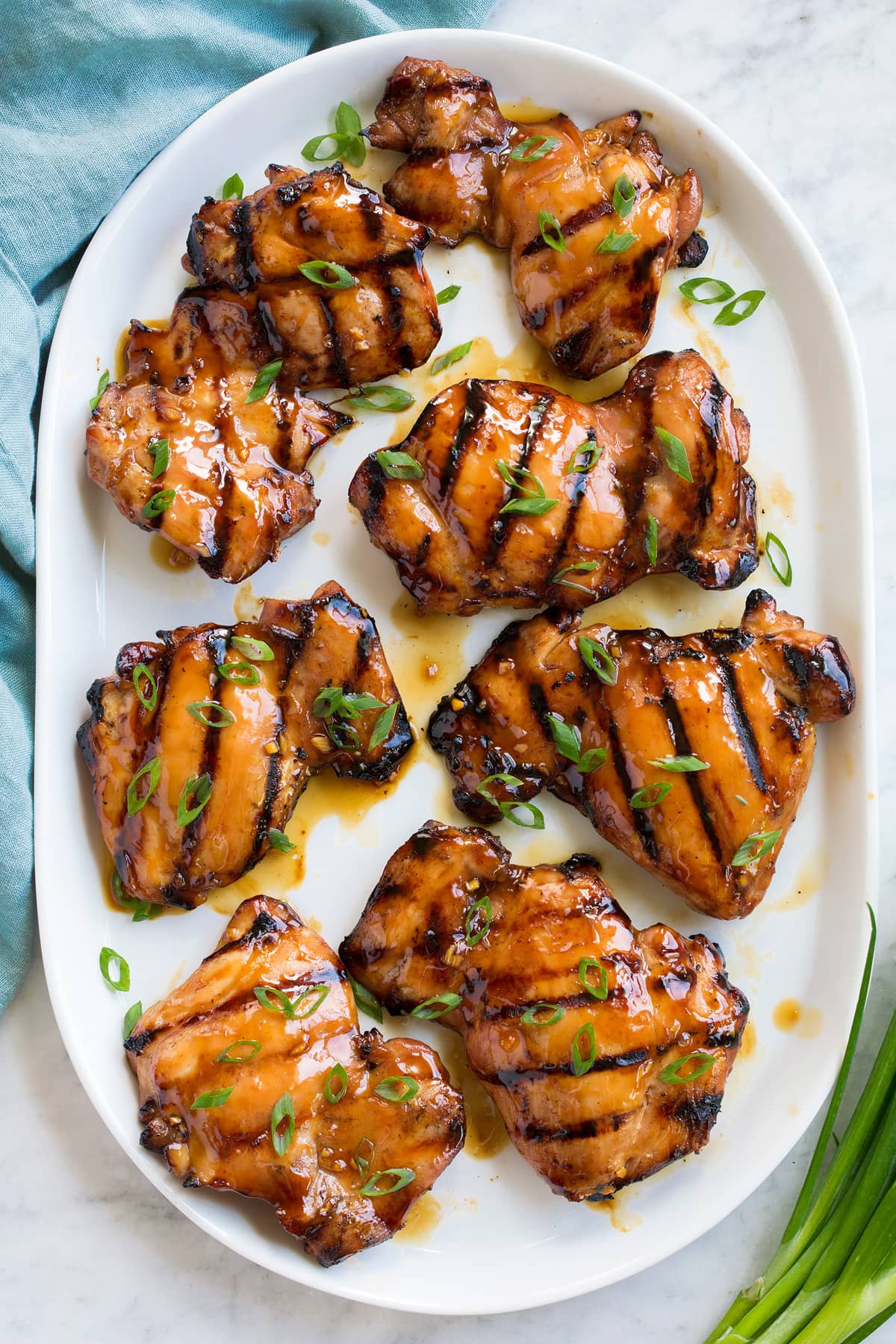 Marinated and grilled teriyaki chicken pieces on a white serving platter, shown overhead.