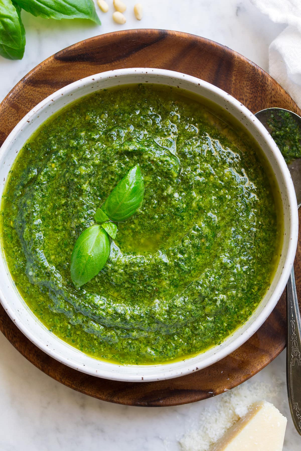 Image shown overhead of pesto in a white bowl resting on a wooden platter.