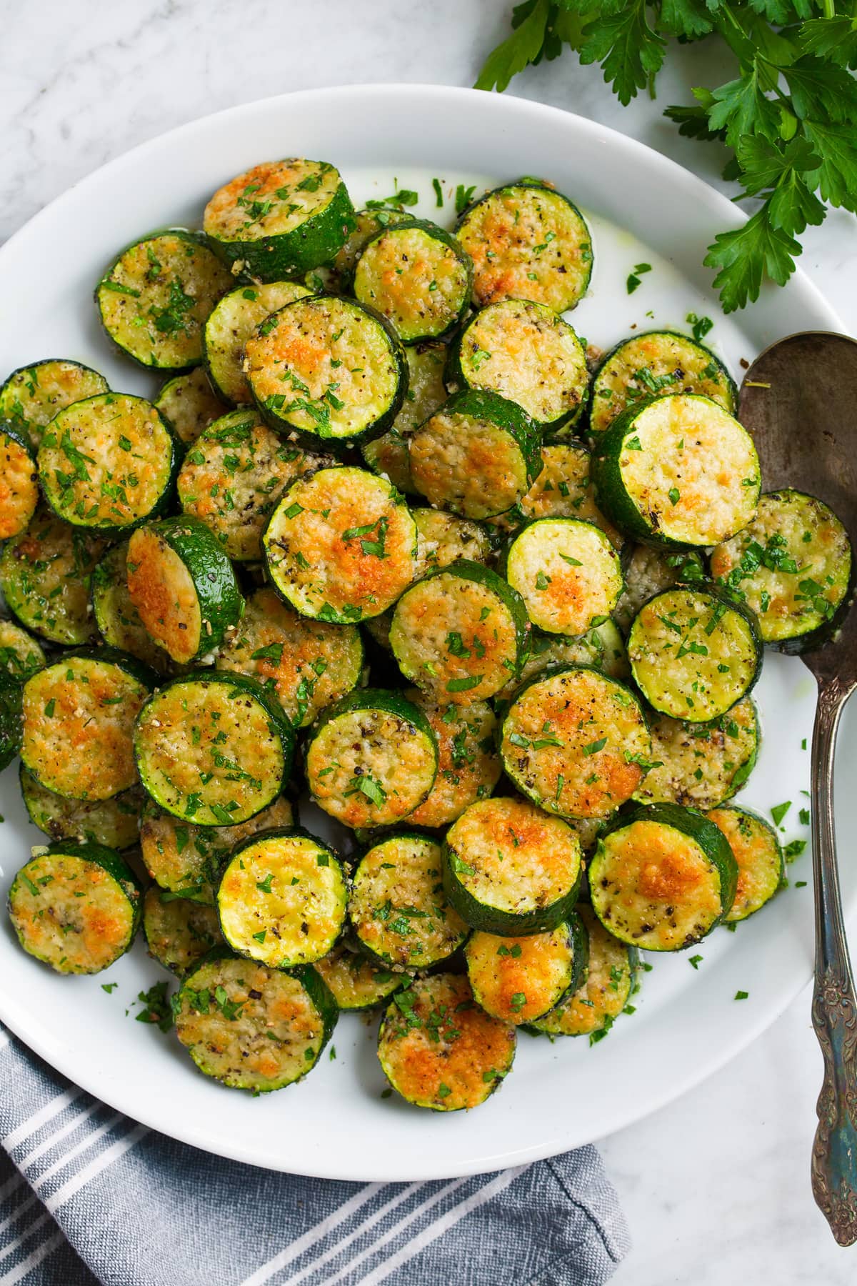 Baked zucchini coins topped with Parmesan displayed high on a white plate.