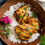 Thai Coconut Grilled Chicken Thighs in a wooden serving bowl with rice and decorative flowers.