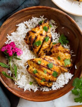 Thai Coconut Grilled Chicken Thighs in a wooden serving bowl with rice and decorative flowers.