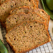 Close up image of sliced zucchini bread on a cutting board with a zucchini and green cloth set to the side.
