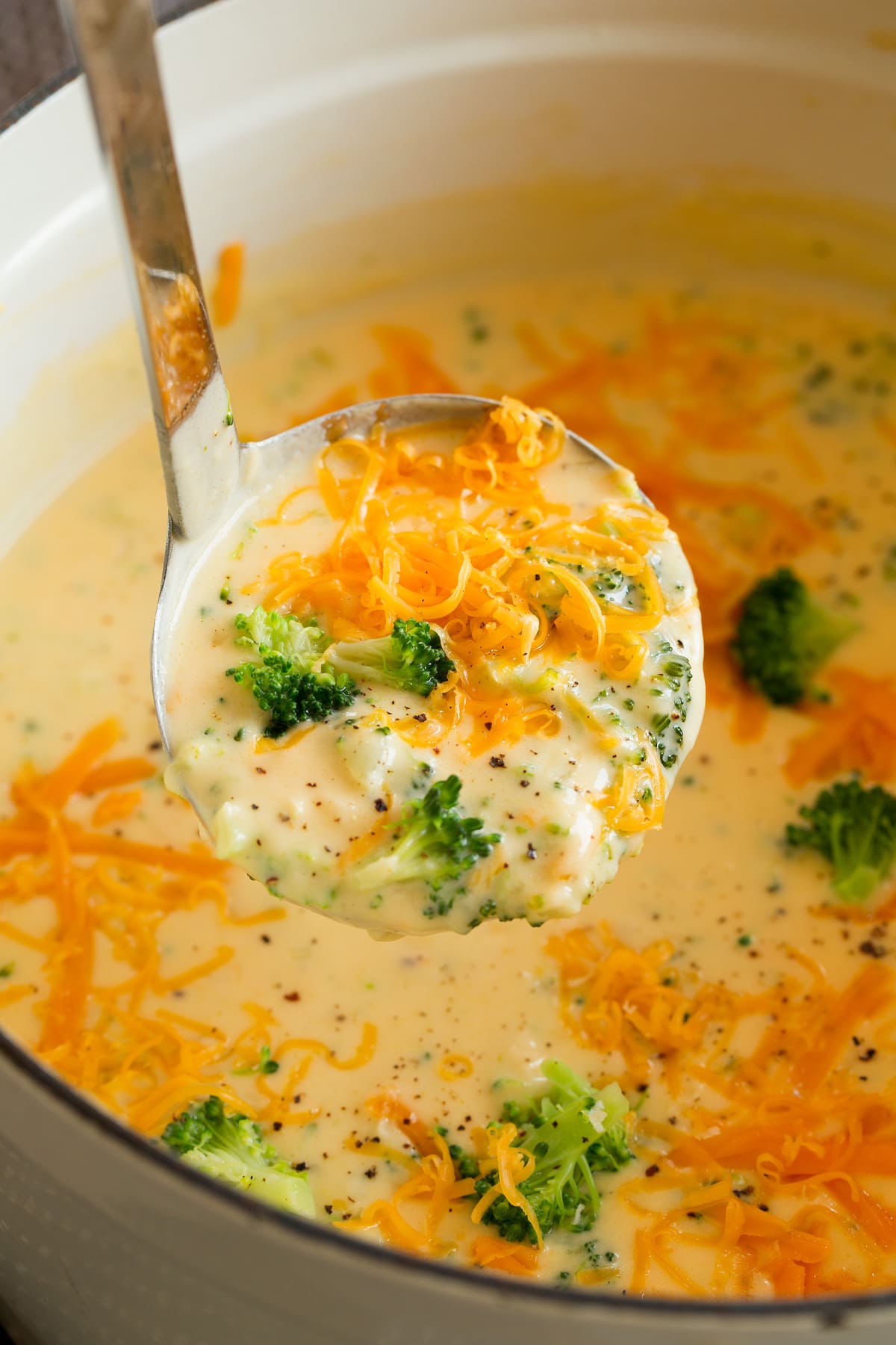 Ladle full of broccoli cheese soup lifted from a pot filled with soup.