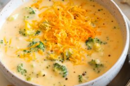 Single serving of broccoli cheese soup in a white bowl with crackers to the side.
