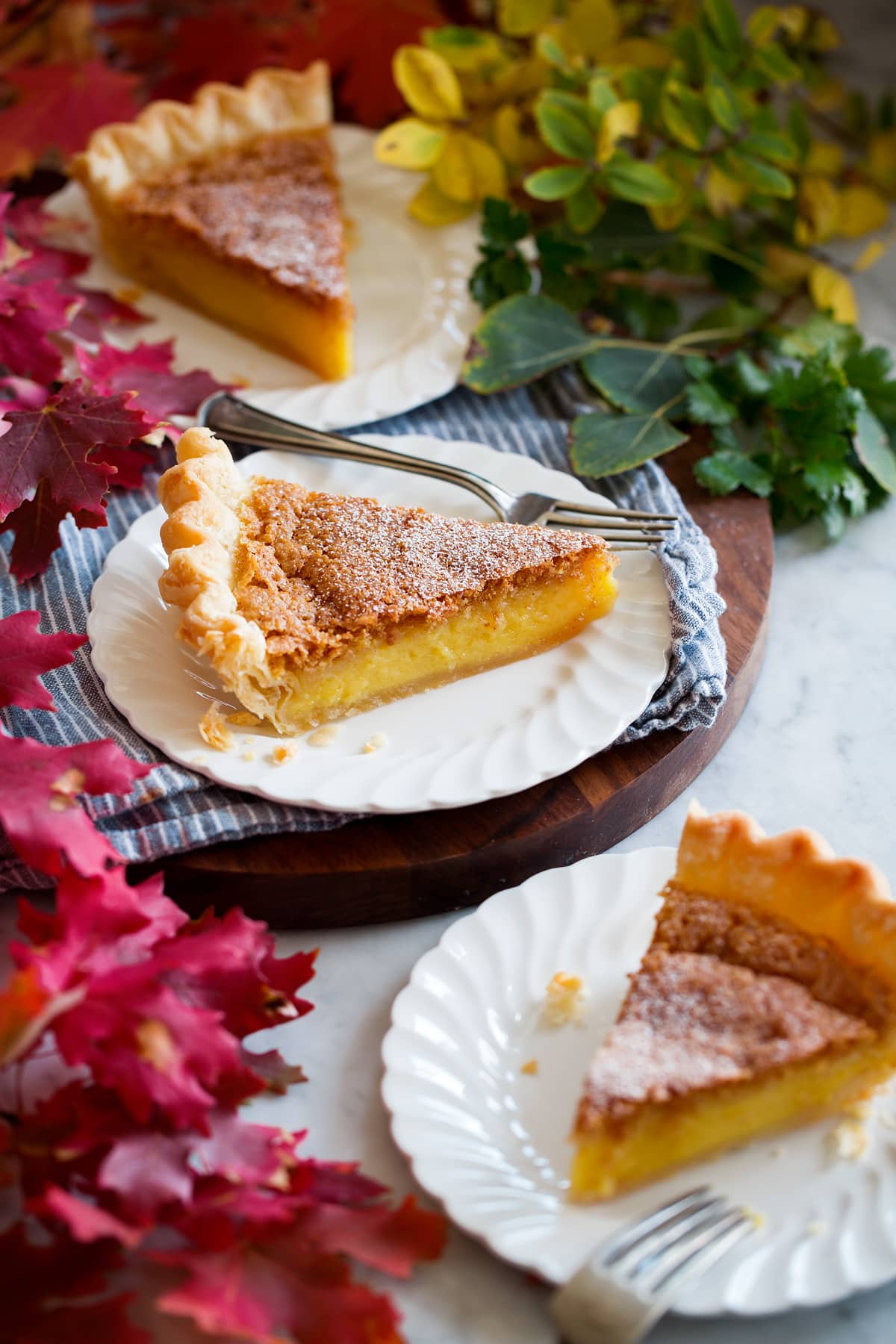 Three slices of chess pie shown on white dessert plates with vibrantly colored fall leaves surrounding.