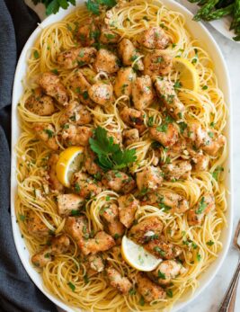 Chicken scampi shown on an oval serving platter. Includes thin spaghetti, lemon, browned chicken pieces and parsley.