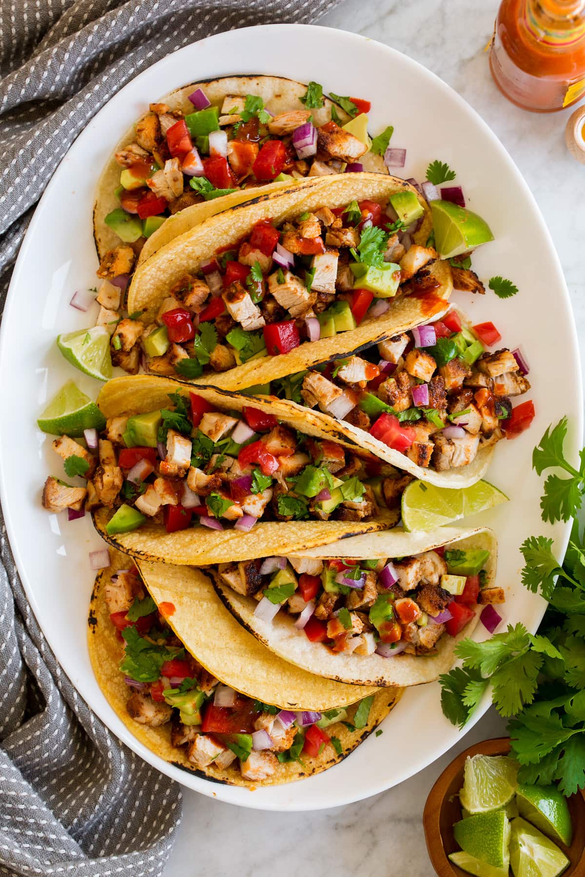 Overhead image of row of six chicken tacos on a white oval serving platter.