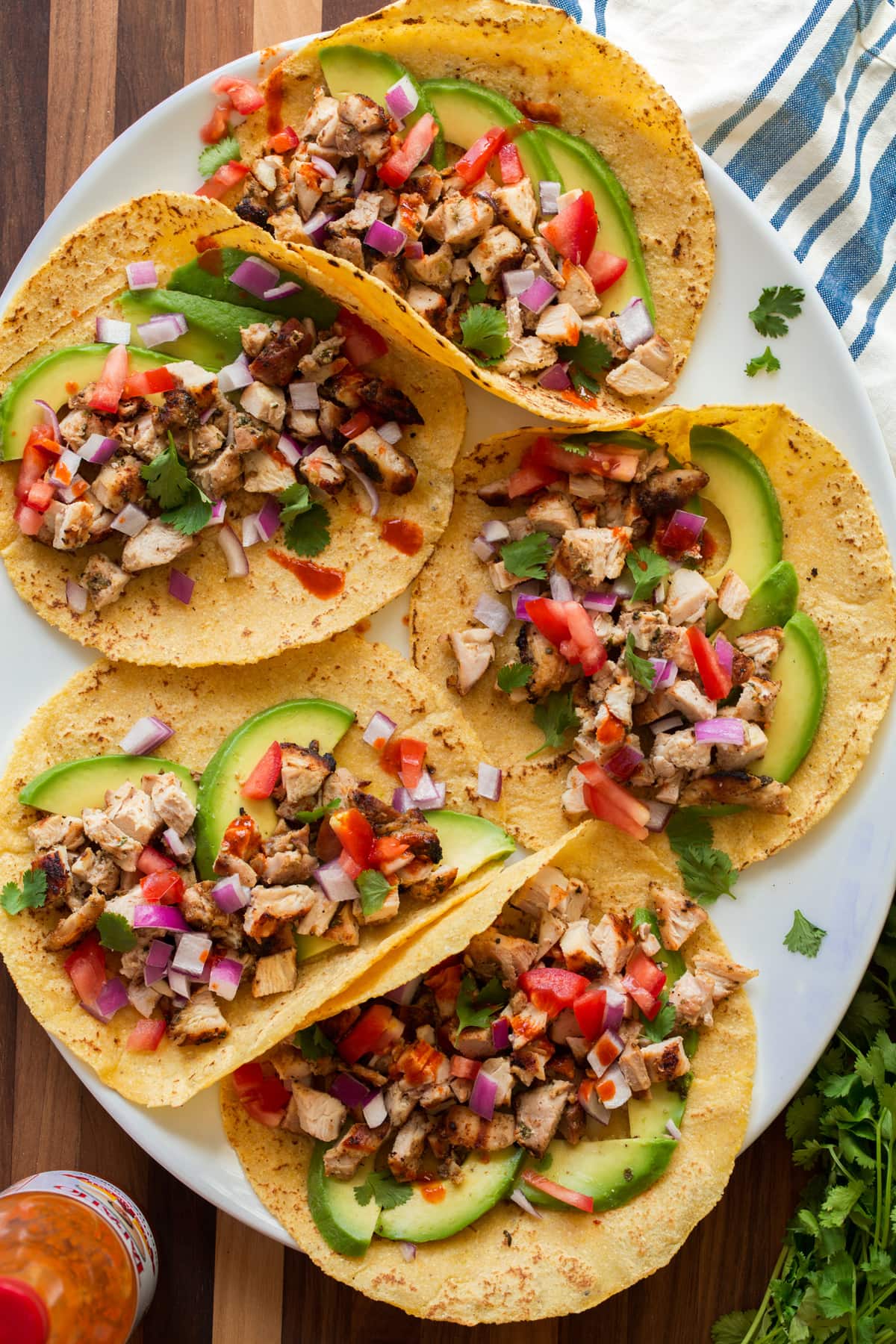 Image of tacos on a platter with homemade tortillas shown. They are topped with diced chicken, avocado, tomato, cilantro and onion.