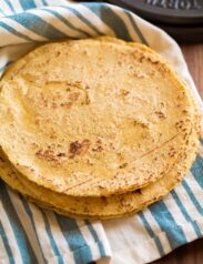 Stack of homemade corn tortillas on a blue striped kitchen towel.