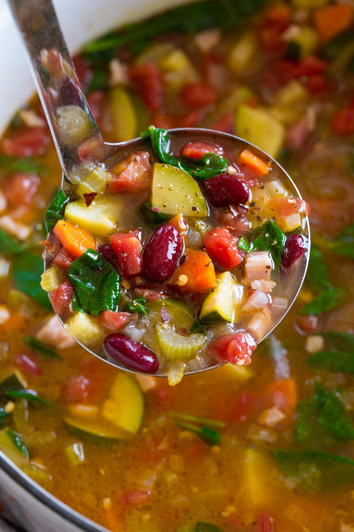 Image of ladle filled with minestrone soup shown close up.