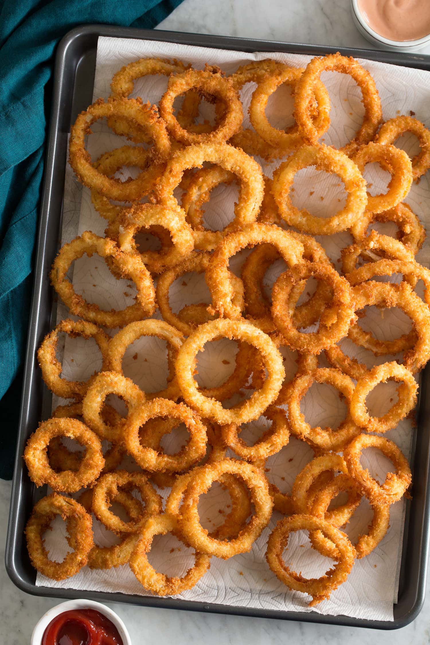Fried onion rings over paper towels on a baking sheet.