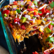 Close up image of slice of layered taco casserole being removed from baking dish.