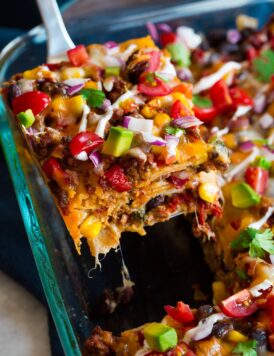 Close up image of slice of layered taco casserole being removed from baking dish.