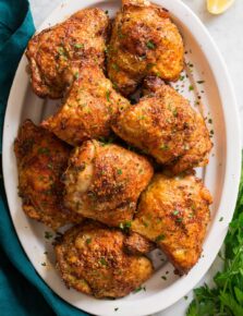 Image of baked chicken thighs shown overhead served on a white oval platter.