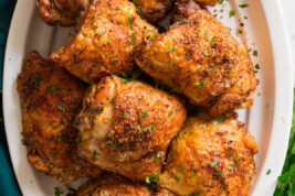 Image of baked chicken thighs shown overhead served on a white oval platter.