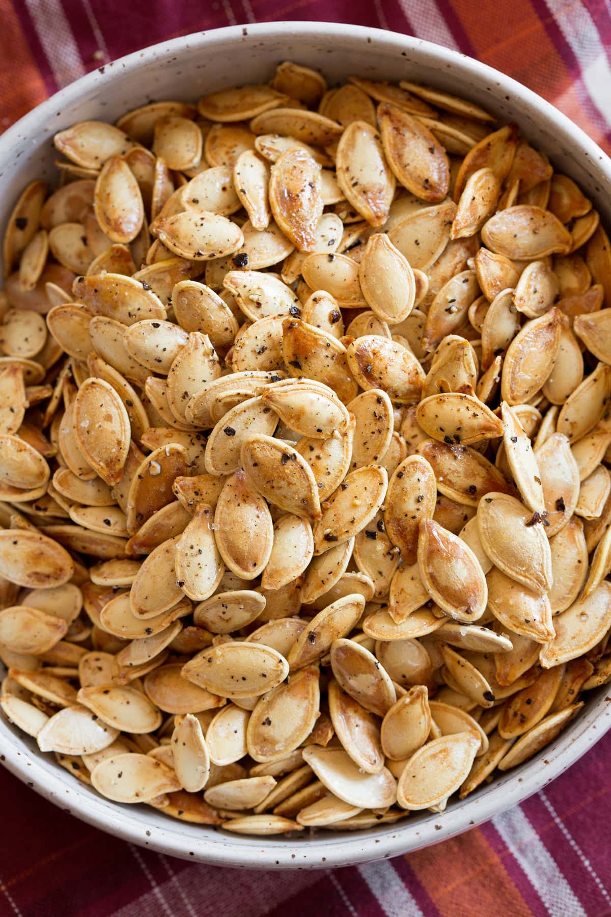 Image of roasted pumpkin seeds shown close up overhead in a white bowl.