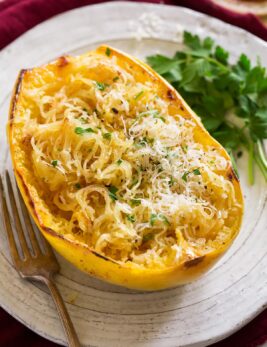 Roasted spaghetti squash half on a white serving plate. Squash it topped with browned butter, parmesan and parsley.