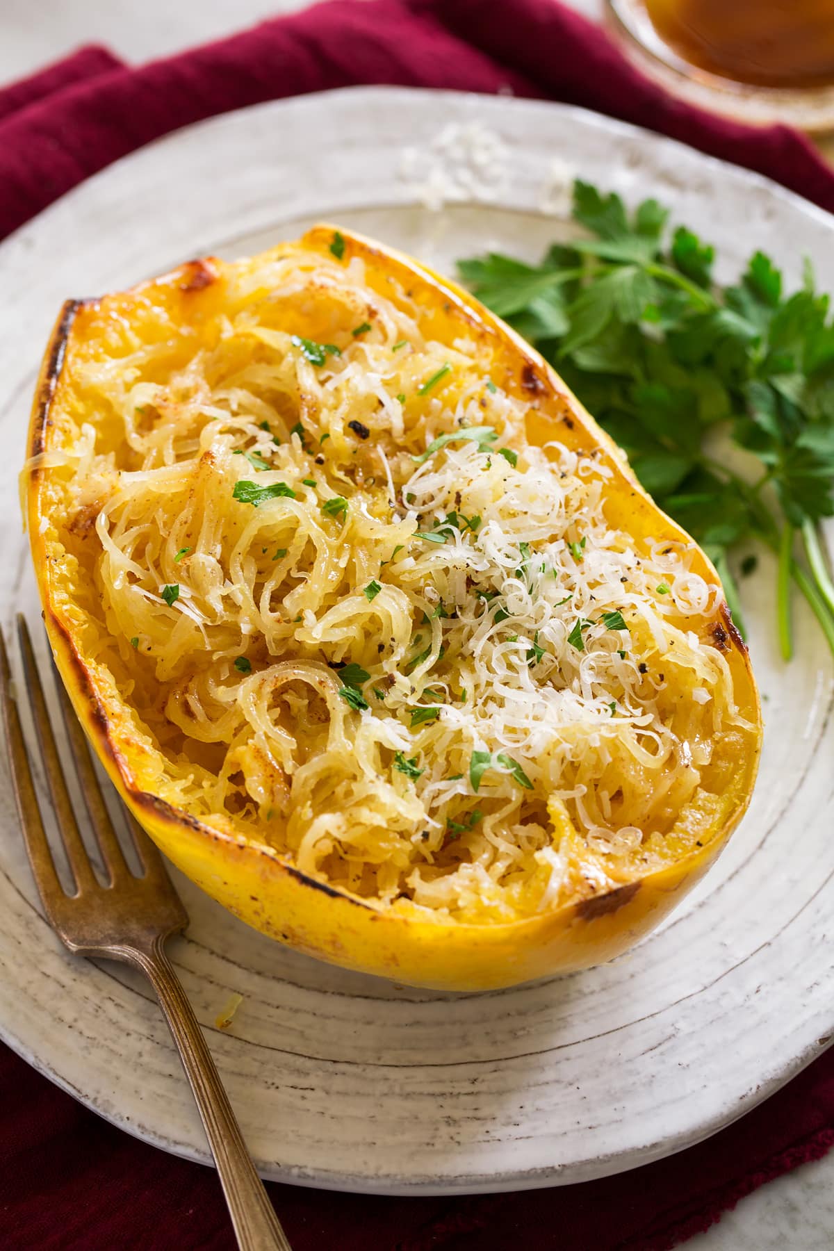 Roasted spaghetti squash half on a white serving plate. Squash it topped with browned butter, parmesan and parsley.
