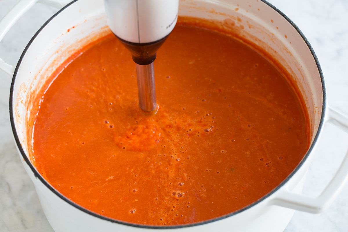 Image of tomato soup being blended with an immersion blender in a pot.