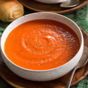 Single serving of tomato soup shown in a white bowl set over a wooden plate.
