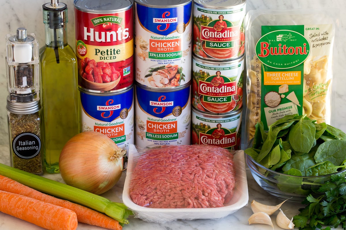 Image of ingredients used to make tortellini soup. Includes cheese tortellini, ground beef, tomatoes, tomato sauce, celery, carrots, onion, garlic, spinach, parsley, olive oil, salt and pepper. 